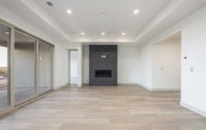 Unfurnished living room featuring a raised ceiling, light wood-type flooring, and a high end fireplace