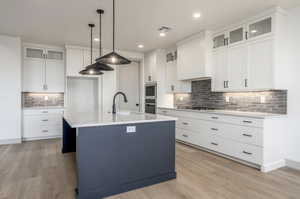 Kitchen with pendant lighting, white cabinets, light hardwood / wood-style flooring, an island with sink, and appliances with stainless steel finishes