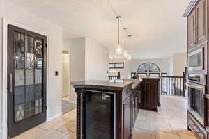 Kitchen with pendant lighting, a kitchen island, dark brown cabinetry, stainless steel appliances, and beverage cooler