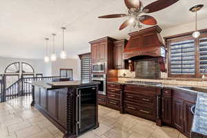 Kitchen featuring appliances with stainless steel finishes, tasteful backsplash, custom range hood, pendant lighting, and wine cooler