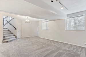 Basement featuring carpet flooring, a chandelier, rail lighting, and a textured ceiling