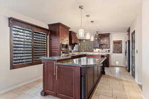 Kitchen featuring tasteful backsplash, stainless steel appliances, decorative light fixtures, dark stone countertops, and a center island