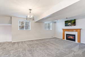 Unfurnished living room with a tiled fireplace, carpet floors, and a notable chandelier