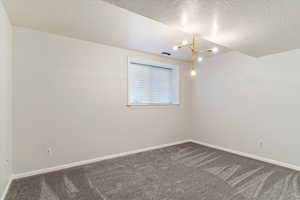 Carpeted spare room featuring a textured ceiling and a chandelier