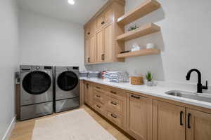 Laundry area with cabinets, washing machine and clothes dryer, sink, and light hardwood / wood-style flooring