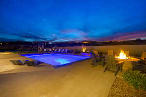 Pool at dusk featuring an outdoor fire pit and a patio