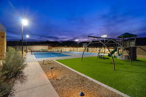 Pool at dusk featuring a playground, a lawn, and tennis court