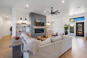 Living room with ceiling fan, a large fireplace, and light hardwood / wood-style floors