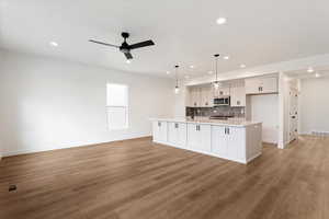 Kitchen with tasteful backsplash, ceiling fan, sink, hanging light fixtures, and an island with sink