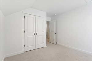 Unfurnished bedroom featuring lofted ceiling, light carpet, and a closet