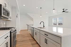 Kitchen with stainless steel appliances, sink, pendant lighting, light hardwood / wood-style flooring, and white cabinets