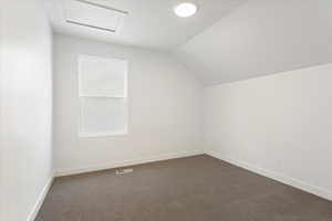 Bonus room featuring dark colored carpet and lofted ceiling