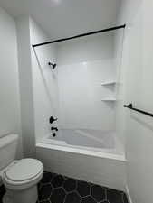 Bathroom featuring tile patterned flooring, tiled shower / bath combo, and toilet