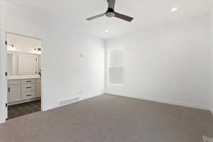 Unfurnished bedroom with ensuite bathroom, ceiling fan, and dark carpet