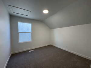 Bonus room featuring dark colored carpet and lofted ceiling