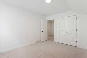 Unfurnished bedroom with a closet, light colored carpet, and lofted ceiling