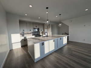 Kitchen featuring appliances with stainless steel finishes, dark hardwood / wood-style flooring, sink, pendant lighting, and an island with sink