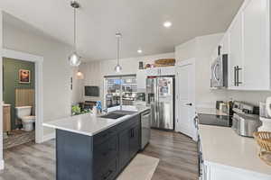 Kitchen featuring stainless steel appliances, a kitchen island with sink, decorative light fixtures, light hardwood / wood-style floors, and white cabinetry