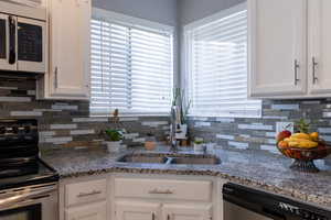 Kitchen featuring dishwasher, white cabinetry, black electric range oven, and sink