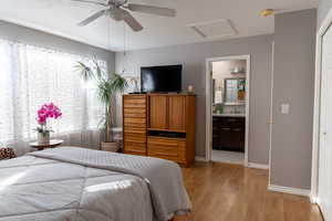 Bedroom featuring ceiling fan, light wood-type flooring, a textured ceiling, and ensuite bath