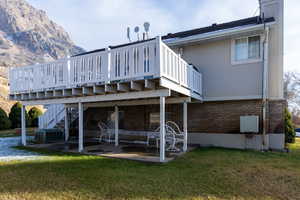 Back of property featuring a patio area, a yard, a deck with mountain view, and central AC