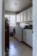 Washroom with cabinets, separate washer and dryer, a textured ceiling, and light tile patterned floors