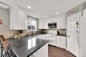 Kitchen featuring white cabinets, dark hardwood / wood-style flooring, white appliances, and kitchen peninsula