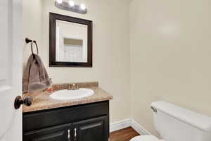 1/2 Bathroom on main with hardwood / wood-style floors, vanity, and toilet