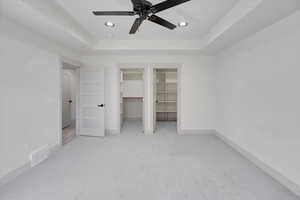 Master bedroom featuring ceiling fan, a raised ceiling, a spacious closet, and light carpet