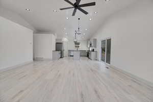 Unfurnished living room with light wood-type flooring, high vaulted ceiling, and ceiling fan