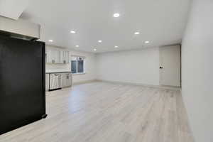 Interior space featuring black refrigerator, light hardwood / wood-style floors, stainless steel dishwasher, and white cabinetry