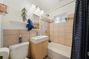 Full bathroom featuring vanity, shower / bath combination with curtain, tile walls, and toilet