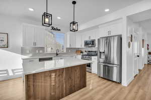 Kitchen with sink, stainless steel appliances, light hardwood / wood-style flooring, decorative light fixtures, and a kitchen island