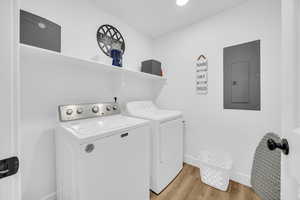 Washroom with washing machine and dryer, light wood-type flooring, and electric panel