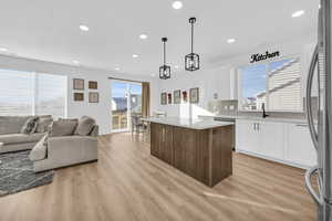 Kitchen with a center island, white cabinets, hanging light fixtures, appliances with stainless steel finishes, and light hardwood / wood-style floors