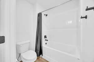 Bathroom with toilet, shower / tub combo with curtain, and hardwood / wood-style flooring