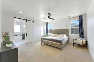 Carpeted bedroom featuring a barn door, ensuite bathroom, multiple windows, and ceiling fan