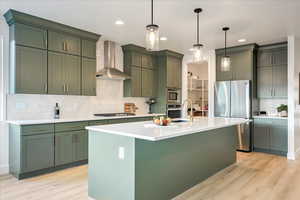 Kitchen featuring appliances with stainless steel finishes, backsplash, light hardwood / wood-style flooring, and wall chimney range hood