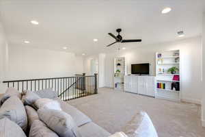 Living room with built in shelves, ceiling fan, and light colored carpet