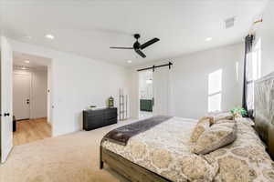 Carpeted bedroom with connected bathroom, a barn door, and ceiling fan