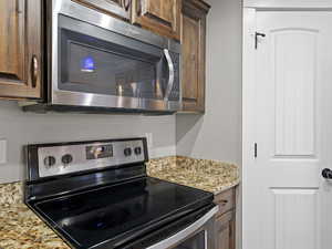 Kitchen with electric range, dark brown cabinets, and light stone countertops