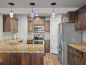 Kitchen featuring appliances with stainless steel finishes, light wood-type flooring, hanging light fixtures, and sink