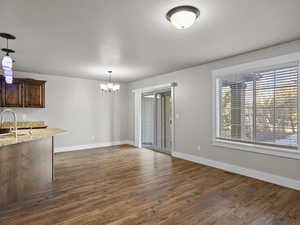 Unfurnished living room with a chandelier, sink, and dark wood-type flooring