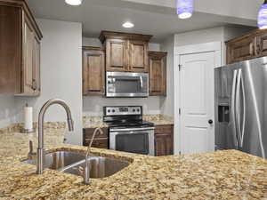 Kitchen featuring appliances with stainless steel finishes, light stone counters, and sink