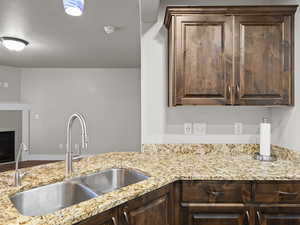 Kitchen featuring dark brown cabinets, light stone countertops, sink, and a brick fireplace