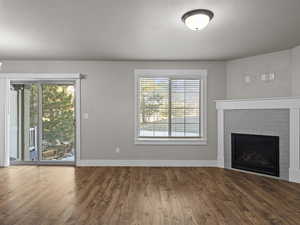 Unfurnished living room with a textured ceiling, hardwood / wood-style flooring, a brick fireplace, and a healthy amount of sunlight