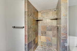 Bathroom featuring tiled shower, a textured ceiling, and toilet