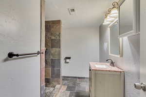 Bathroom with vanity, a textured ceiling, and tiled shower