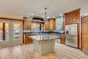 Kitchen featuring dark stone counters, hanging light fixtures, light hardwood / wood-style floors, appliances with stainless steel finishes, and a kitchen island