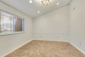 Carpeted spare room featuring vaulted ceiling